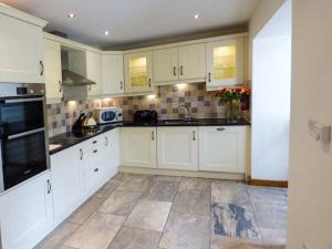 uma cozinha com armários brancos e piso em azulejo em Ghyll Bank Cow Shed em Staveley