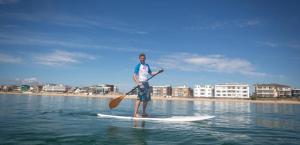 a man is standing on a paddle board in the water at Top Floor Sandbanks Apartment with Free Parking just minutes from the Beach and Bars in Canford Cliffs