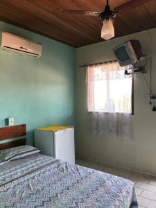 a bedroom with a bed and a refrigerator and a window at Pousada Encanto da Ilha in Praia de Araçatiba