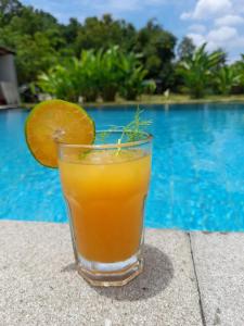 a glass of orange juice sitting on a table next to a pool at Tree Tops Mandalika in Kuta Lombok