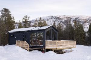 a black cabin in the snow with mountains in the background at Flatmoen Natur Lodge in Alta