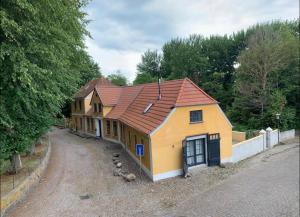 a yellow house with a red roof on a dirt road at Historisches Pastorat - Villa Mika in Fehmarn