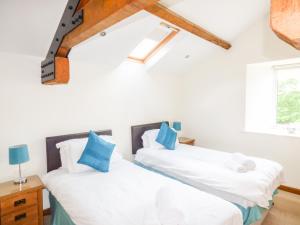 two beds in a room with white walls and blue pillows at Ghyll Bank Byre in Staveley