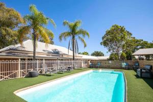 a swimming pool with palm trees and a house at Nightcap at Macquarie Inn in Dubbo