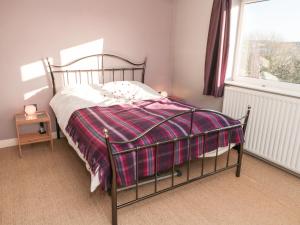 a bedroom with a bed with a plaid blanket on it at Jasmine Cottage in Bakewell