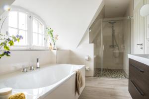 a white bathroom with a large tub and a shower at Ferienhaus Seeadler 7 in Fuhlendorf +21 photos