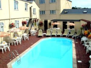 een zwembad met stoelen, tafels en parasols bij Ashley Court Hotel in Torquay