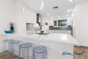 a white kitchen with three bar stools and a sink at 35 Degrees South by Wine Coast Holiday Rentals - Escape to the fabulous 35 Degrees South by Wine Coast Holiday Rentals. in Port Noarlunga