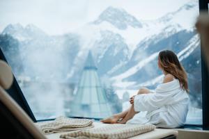 a woman in a white dress sitting on a window with mountains at Aqua Dome 4 Sterne Superior Hotel & Tirol Therme Längenfeld in Längenfeld