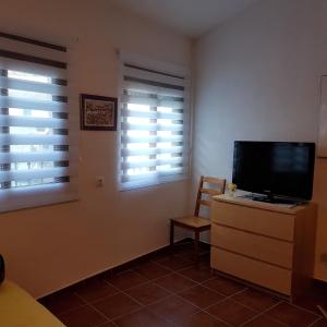 um quarto com uma televisão numa cómoda e duas janelas em Casa Alameda em Benarrabá