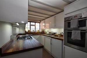 uma cozinha com armários brancos e um forno com placa de fogão em Rose Mullion Cottage em Pett