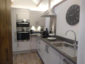 a kitchen with white cabinets and a clock on the wall at The Nook Cottage In The Heart Of Northumberland in Wark