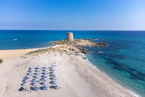 - un groupe de parasols et de chaises sur une plage avec un phare dans l'établissement Hotel la Torre, à Bari Sardo