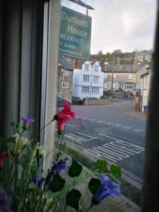 una ventana de una casa con flores púrpuras y una calle en Durham House, en Beer