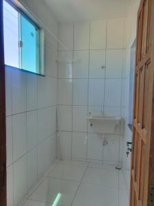 La salle de bains est pourvue de carrelage blanc, d'un lavabo et d'une fenêtre. dans l'établissement Apartamento Próximo da Praia em Cabo Frio, à Cabo Frio
