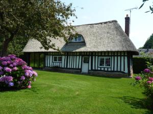 a cottage with a thatched roof and flowers at Gite La Charretterie in Omonville