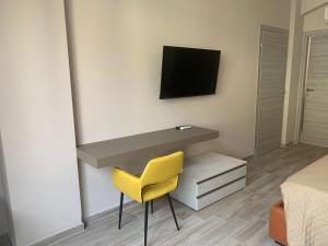 Una silla amarilla en una habitación con escritorio y TV. en Tripepi suites, en Reggio Calabria