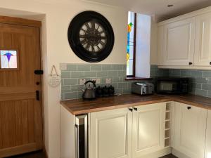 una cocina con armarios blancos y un reloj en la pared en 3 Bed Detached Cottage- Log Burner Mountain Views, en Beaumaris