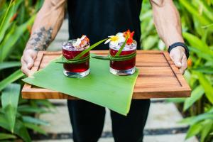 a man holding a tray with two cocktails on it at Mother Earth Luxury Boutique Hotel, Restaurant & Spa in Tamarindo