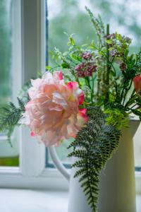 um vaso branco com flores cor-de-rosa numa janela em The Sunshine Annex at Lower Fields Farm em Napton on the Hill