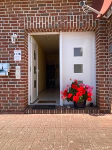 a brick building with a door with a pot of red flowers at Ferienwohnungen Koch EG adult only in Wangerland