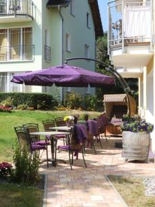 un patio con tavoli, sedie e ombrellone viola di Pension Delia Will a Ahlbeck