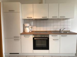 cocina con armarios blancos, fregadero y fogones en Apartments Schnepel, en Sankt Michaelisdonn