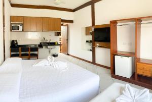 a bedroom with a large white bed and a kitchen at Suítes Trilha do Sol in Ubatuba