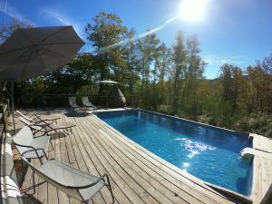 a pool with chairs and an umbrella on a wooden deck at Estiva - Le Chalet Belvédère - Piscine, Spa, Vue Grandiose in Lapeyrugue