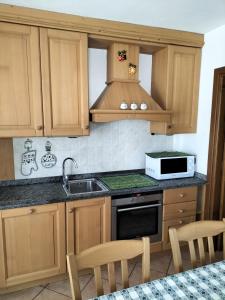 cocina con armarios de madera, fregadero y microondas en Baita Rutic, en Oga