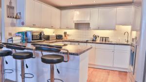 a kitchen with white cabinets and bar stools at Harbourside Apartment in Mevagissey