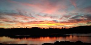 un coucher de soleil sur une étendue d'eau plantée d'arbres dans l'établissement Les balcons du lac, à Malbuisson