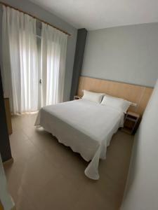 Un dormitorio con una gran cama blanca y una ventana en Hostal Manuela, en Punta Umbría