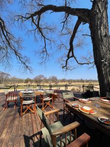 eine Holzterrasse mit Tischen, Stühlen und einem Baum in der Unterkunft Ngangane Lodge & Reserve in Francistown