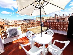 una mesa blanca y sillas en un balcón con sombrilla en Casa de Huéspedes Vecinodecerbantes en Alcalá de Henares