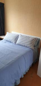 a bed with blue sheets and pillows on it at Urenui Beach Bach in Urenui