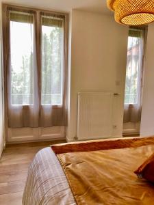 a bedroom with two windows and a bed in it at La Maison, 4 appartements 3 étoiles climatisés au centre ville avec jardin proche du Parc et des Thermes in Lons-le-Saunier