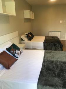 two beds in a hotel room with white sheets at Piavi Residencial in São Francisco de Paula