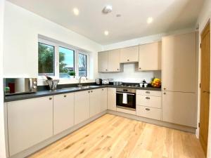 a kitchen with white cabinets and a wooden floor at NEW Beautiful Large 3 bedroom House - 5 Minutes to the nearest Beach! - Great Location - Garden - Parking - Fast WiFi - Smart TV - Newly decorated - sleeps up to 7! Close to Poole & Bournemouth & Sandbanks in Lytchett Minster