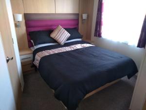 a bedroom with a large bed with a pink headboard at E3 is a 2 Bedroom 6 berth Lodge on Whitehouse Leisure Park in Towyn near Rhyl close to beach with decking and private parking space This is a pet free caravan in Rhyl