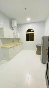 a kitchen with white cabinets and a white tile floor at همس العلا للشقق المفروشة in AlUla