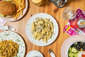a table topped with plates of food with pasta and a hamburger at Safestay Pisa Centrale in Pisa