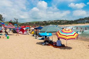 a group of people sitting under umbrellas on a beach at La Saville BnB in Scottburgh