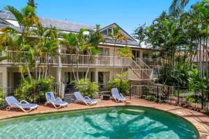 a swimming pool in front of a house with chairs and a house at Byron Bay Beach Apartments in Byron Bay