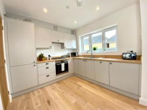 a kitchen with white cabinets and a wooden floor at Stunning NEW Large 3 bedroom House - 5 Minutes to the nearest Beach! - Great Location - Garden - Parking - Fast WiFi - Smart TV - Newly decorated - sleeps up to 7! Close to Poole & Bournemouth & Sandbanks in Lytchett Minster +10 photos