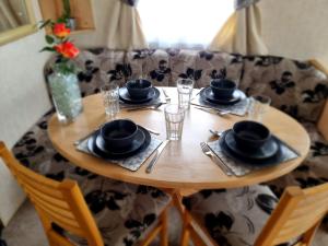 a wooden table with plates and glasses on top of it at 3 Bedroom Sleeps 6 on Coral Beach in Ingoldmells