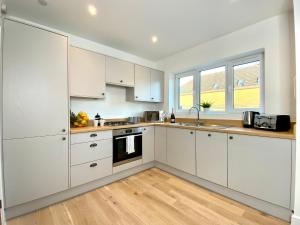 a white kitchen with white cabinets and a wooden floor at Amazing NEW Large 2 bedroom House - 5 Minutes to the nearest Beach! - Great Location - Garden - Parking - Fast WiFi - Smart TV - Newly decorated - sleeps up to 5! Close to Poole & Bournemouth & Sandbanks in Lytchett Minster
