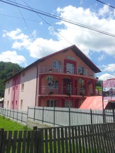 a red and white building with a fence in front of it at Pensiunea Floare de Bucovina in Frasin