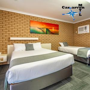 a bedroom with two beds and a brick wall at Carnarvon Motel in Carnarvon
