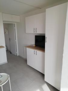 um quarto com uma cozinha com armários brancos e uma televisão em Le Miroir de la mer em Saint-Aygulf